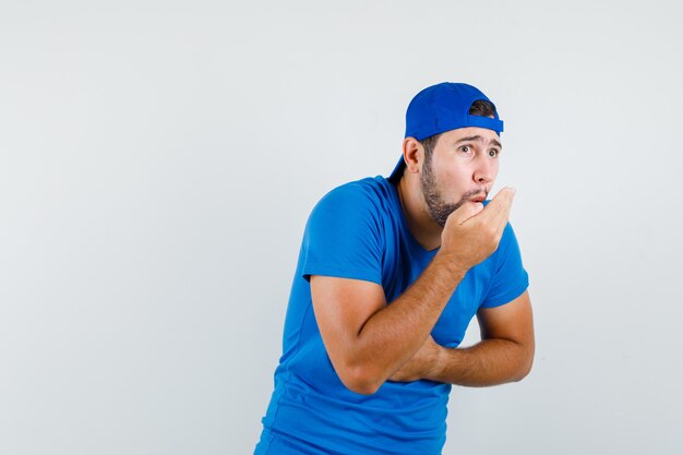 Young man in blue t-shirt and cap whistling by holding breath