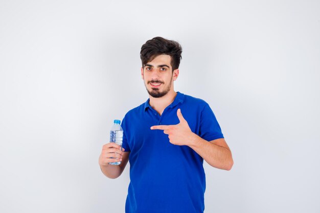 Young man in blue t-shirt holding water bottle and pointing to it with index finger and looking optimistic