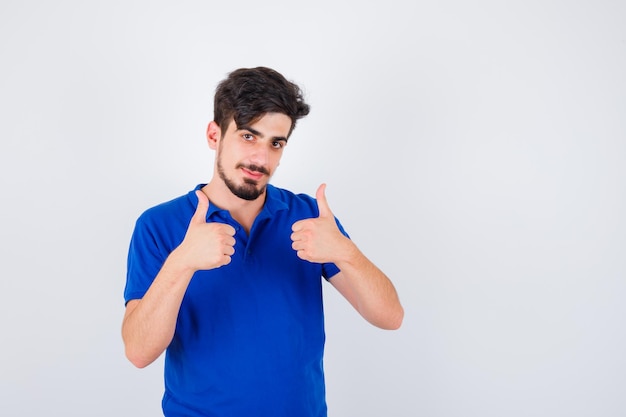 Молодой человек в синей футболке показывает палец вверх обеими руками и выглядит счастливым