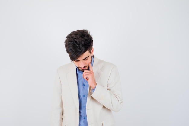 Young man in blue t-shirt and white suit jacket putting hand on chin, thinking about something and looking pensive