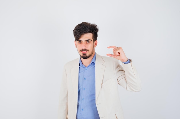 Young man in blue t-shirt and white suit jacket stretching one hand as holding something small and looking serious