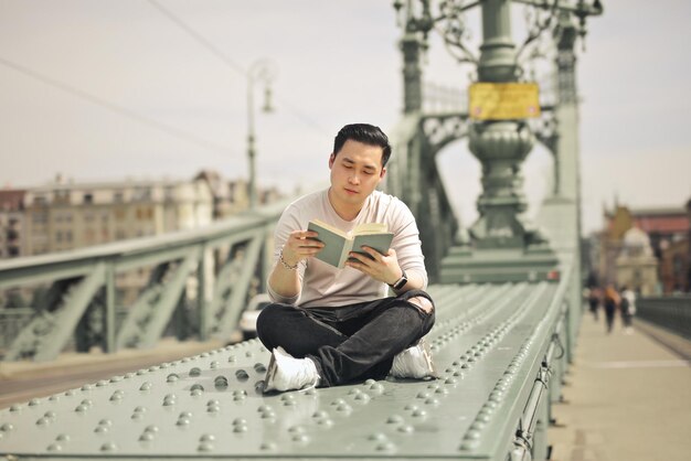 young man on a bridge reads a book