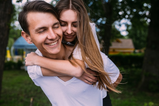 Young man carries his girlfriend on his back in the park