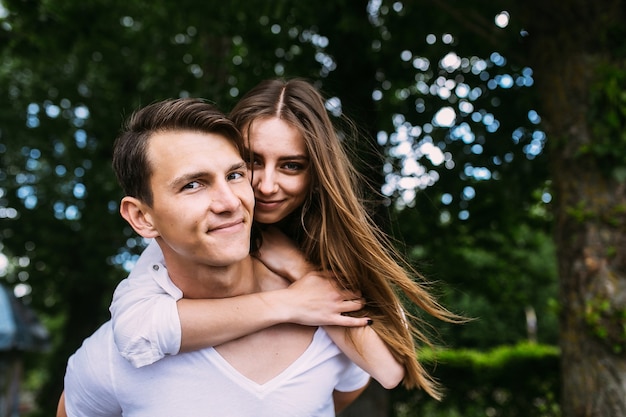 Young man carries his girlfriend on his back in the park