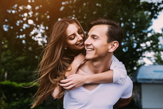 Young man carries his girlfriend on his back in the park