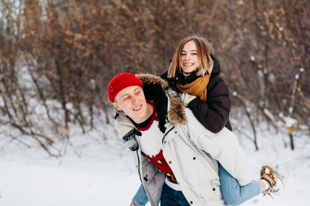 Young man carrying woman on back in winter forest 