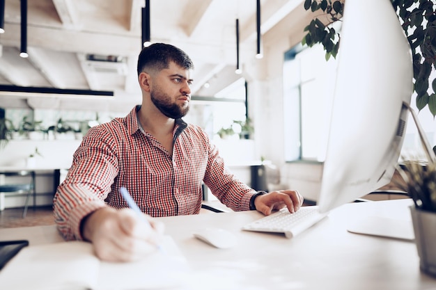 Young man in casual shirt working on computer in office