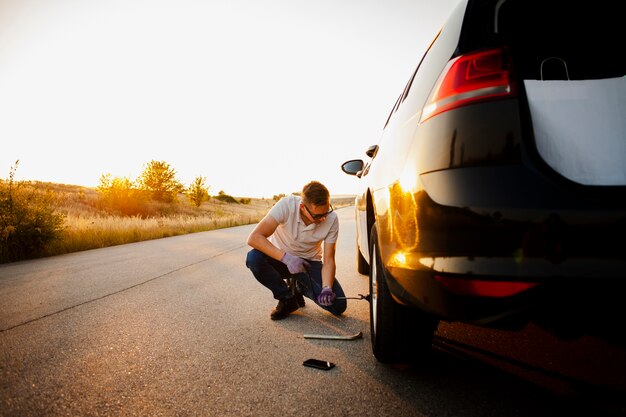 若い男が車のホイールを変更します