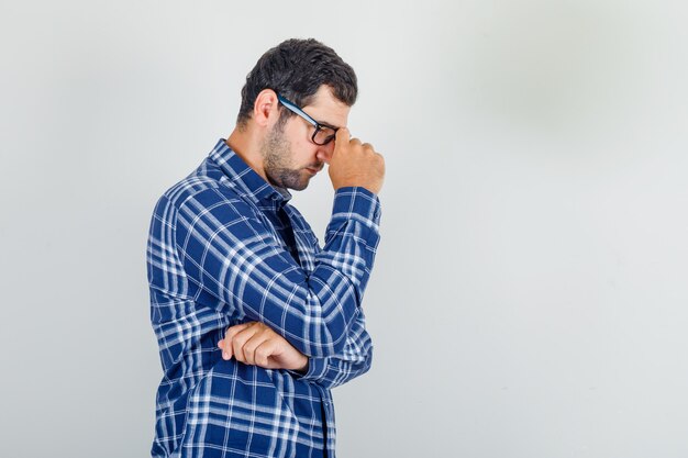 young man in checked shirt, glasses looking down and thinking and looking sad