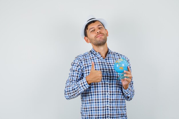 Young man in checked shirt, hat holding globe