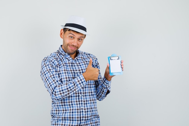 Young man in checked shirt, hat holding mini clipboard