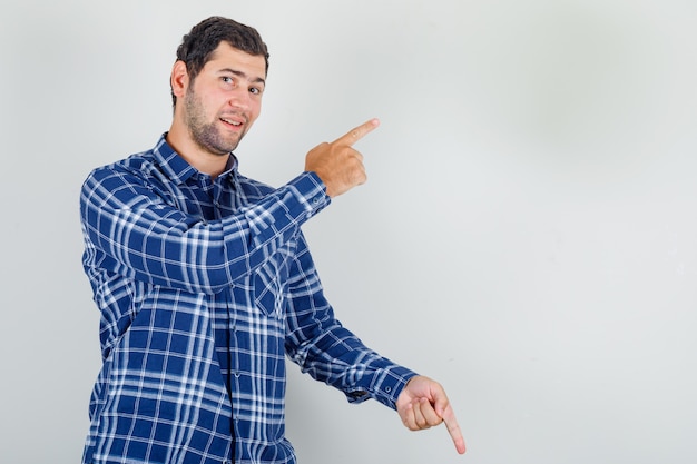 Giovane uomo in camicia a quadri che punta le dita su e giù e sembra felice