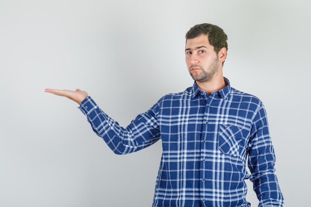 Young man in checked shirt showing something or welcoming with hand