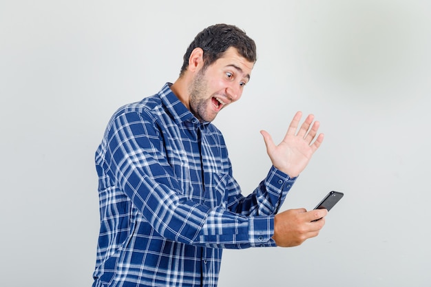 Giovane uomo in camicia a quadri agitando la mano sulla videochiamata e guardando felice