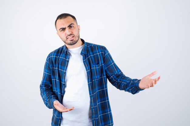 Young man in checked shirt and white t-shirt stretching hands as receiving something and looking annoyed