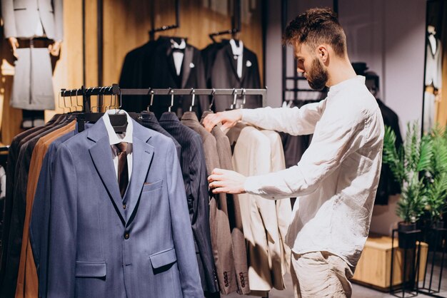 Молодой человек выбирает одежду в магазине мужской одежды