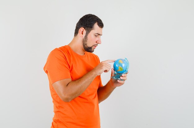オレンジ色のTシャツで地球上の目的地を選択し、焦点を当てた、正面図を探している若い男。