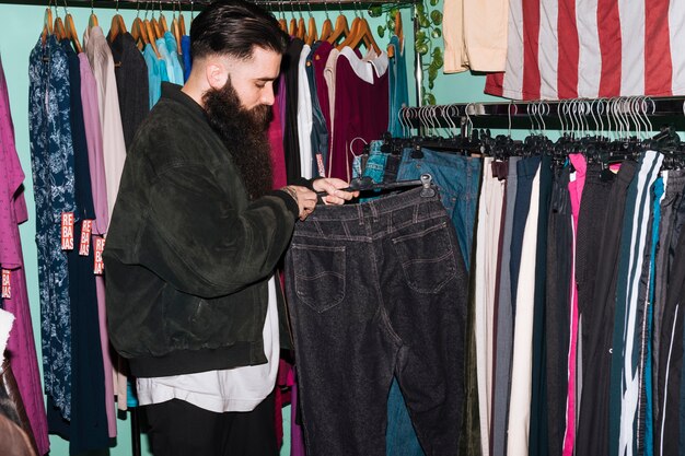 Молодой человек выбирая джинсы вися на рельсе в магазине одежды