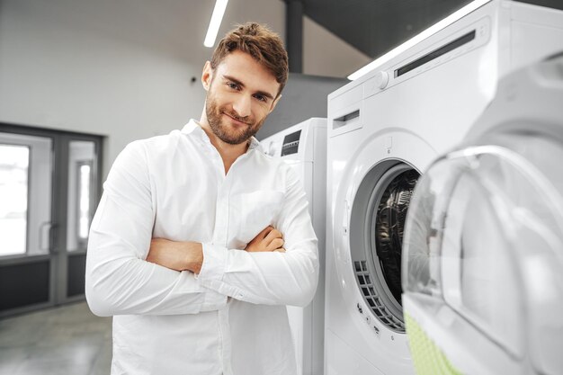 Young man choosing new washing machine in household appliances store