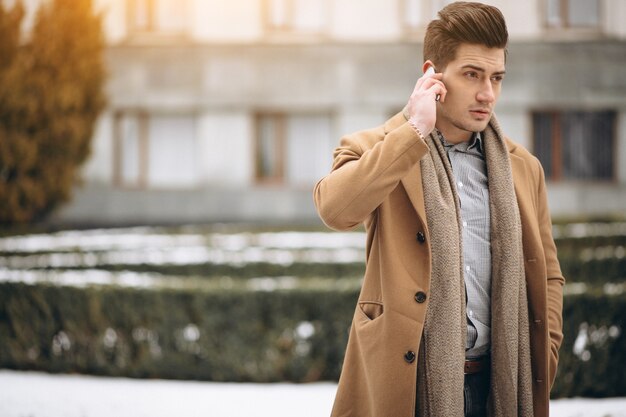 Young man in coat talking on the phone outside