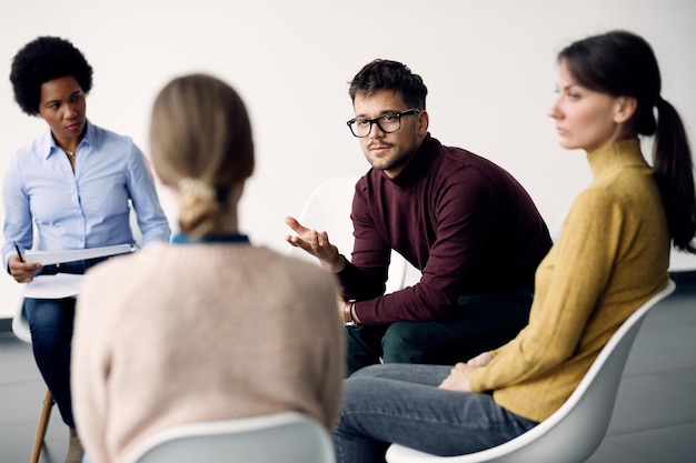 Young man communicating with participants of group therapy at community center