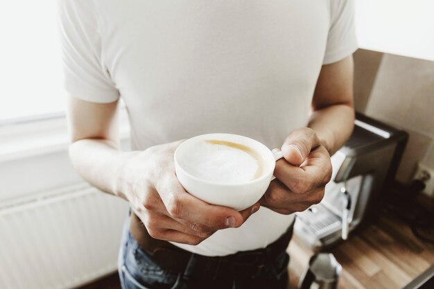 若い男が自宅で自動coffeemachineでコーヒーを調理します。
