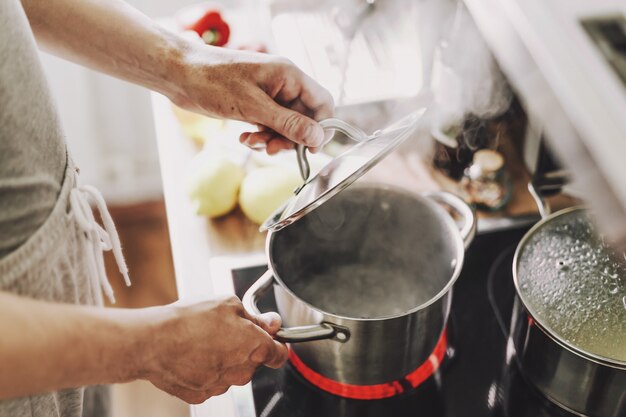 Молодой человек варя свежие продукты дома и раскрывая крышку испаряясь бака.