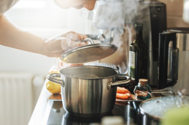 若い男が自宅で新鮮な食品を調理し、蒸し鍋の蓋を開きます。