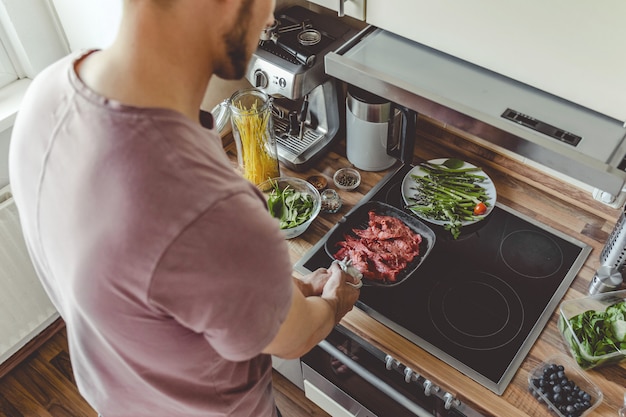 Young man cooking raw meat on grill pan