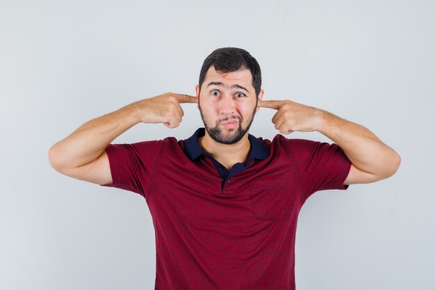 Young man covering ears with his fingers in red t-shirt and looking calm , front view.