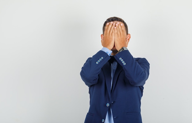 Young man covering face with hands in suit and looking regretful