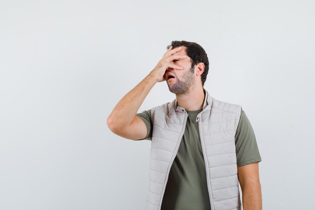 Young man covering his face with hands on white background