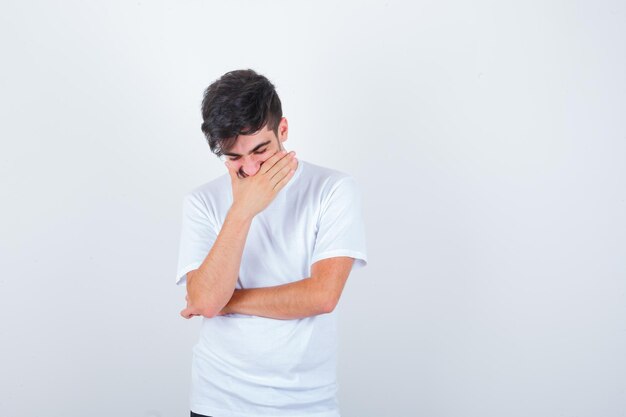 Young man covering mouth with hand in t-shirt and looking happy