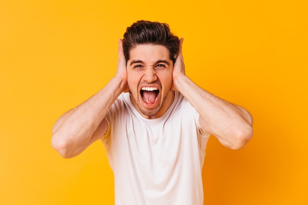 Free photo young man covers his ears with his hands and shouts loudly on orange space.