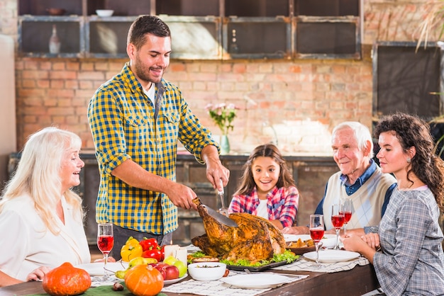 Young man cutting baked chicken at table with family
