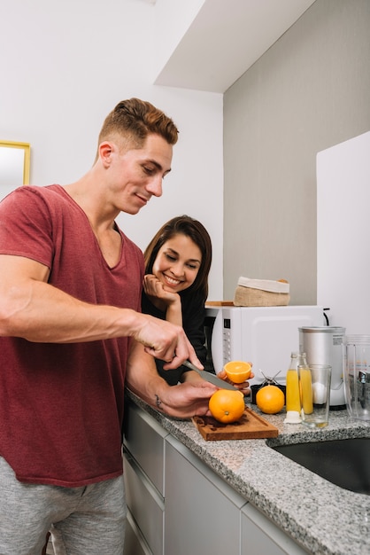 Young man cutting orange in kitchen with woman