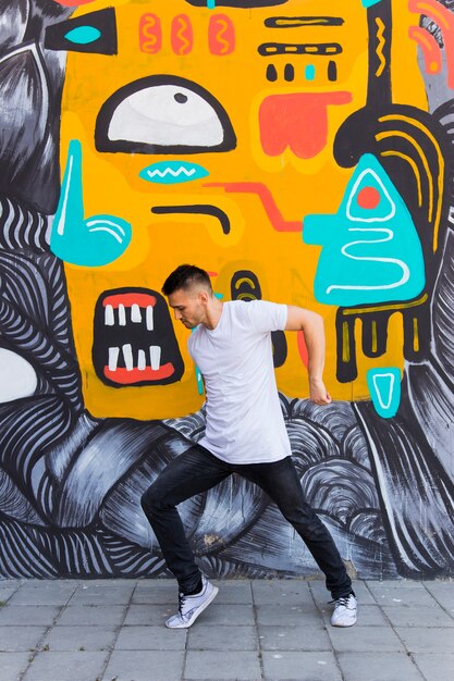 Young man dancing against graffiti wall