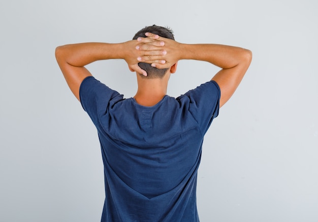 Free photo young man in dark blue t-shirt crossing hands behind head and looking relaxed, back view.