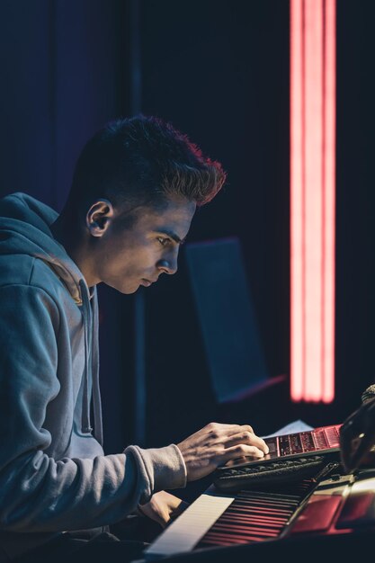 Young man in a dark room at the music keys with a laptop