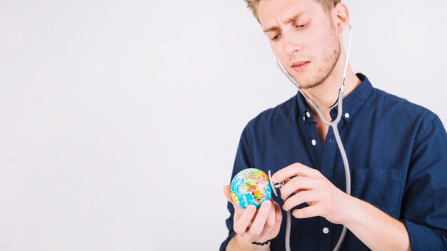 Young man diagnosing globe with stethoscope