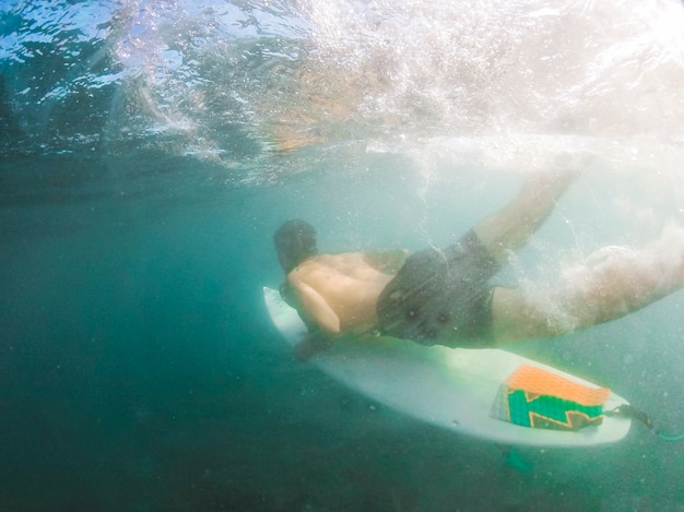 Young man diving with surfboard underwater