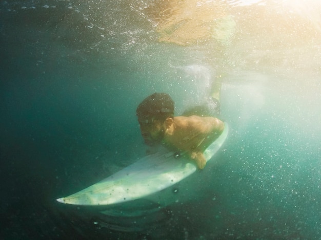 Young man diving with white surfboard underwater