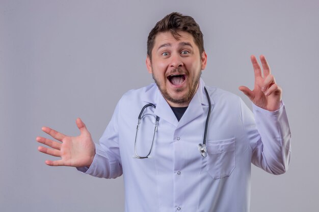 Young man doctor wearing white coat and stethoscope looking very surprised and happy