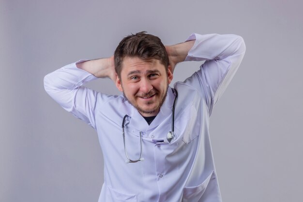 흰색 코트와 청진기를 착용하는 젊은 남자 의사는 하루 종일 일하고 스트레칭 된 위치에 팔을 스트레칭 미소