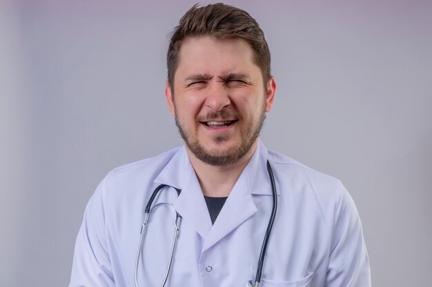 Young man doctor wearing white coat and stethoscope  and squinting