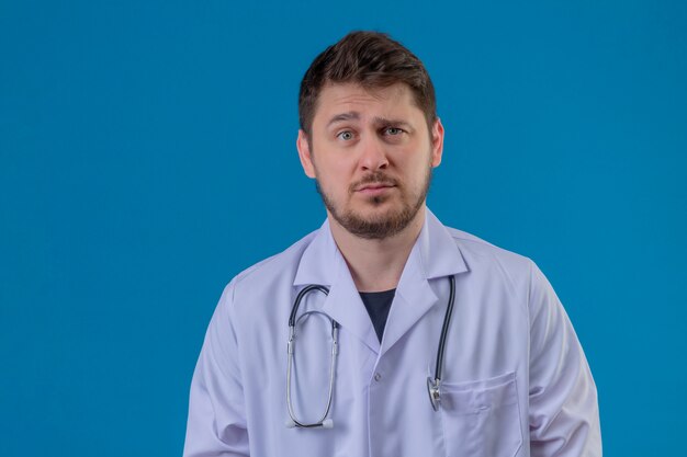 Free photo young man doctor wearing white coat and stethoscope standing with skeptic facial expression over isolated blue background