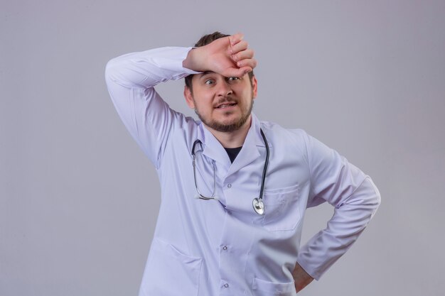 Young man doctor wearing white coat and stethoscope surprised with hand on head for mistake, bad memory concept 1