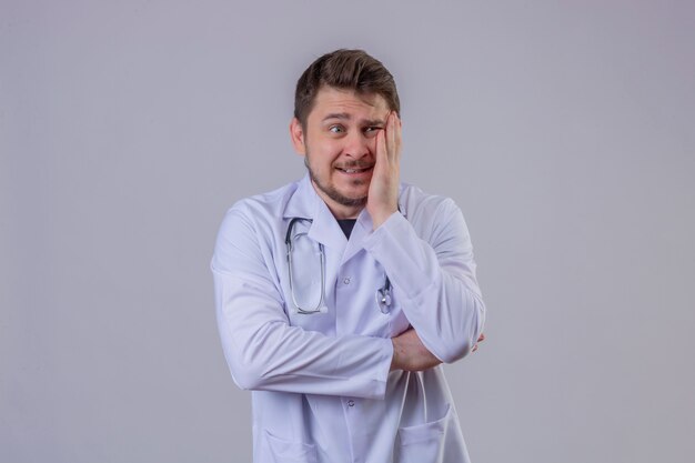 Young man doctor wearing white coat and stethoscope worried or frightened look, looking to the side