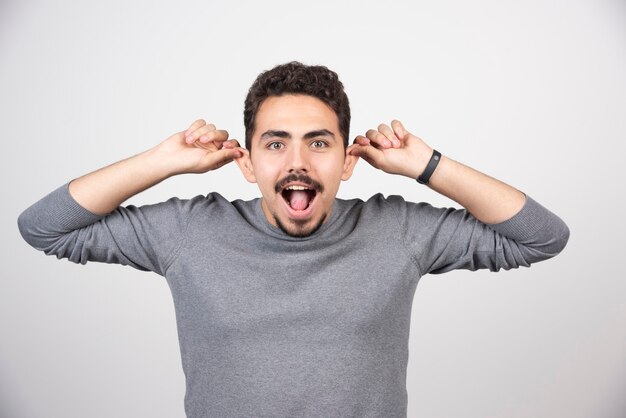 A young man doing a funny face over a white wall.