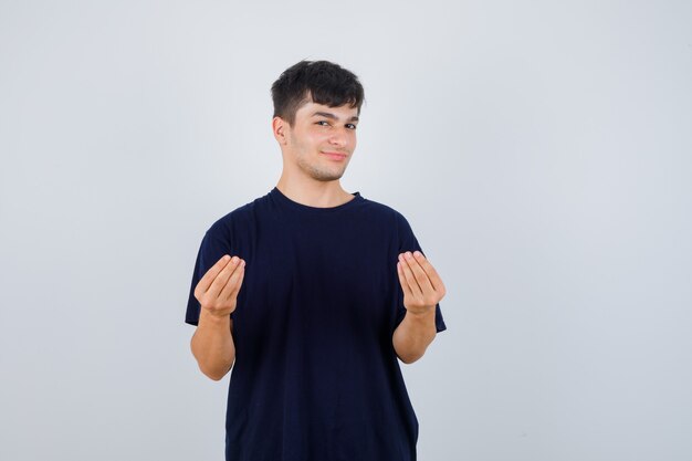 Молодой человек делает итальянский жест в черной футболке и выглядит уверенно, вид спереди.